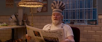Movie still from “Paddington 2” (2017), directed by Paul King – An old man wearing a chef hat and holding a newspaper; Medium shot, High angle
