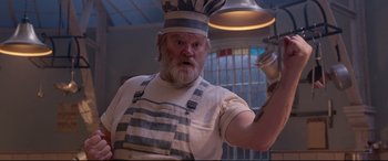 Movie still from “Paddington 2” (2017), directed by Paul King – An old man wearing a chef's hat holding a pan; Medium shot, Low angle