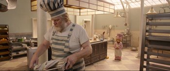 Movie still from “Paddington 2” (2017), directed by Paul King – An old man in a striped apron is holding a newspaper; Wide shot, Low angle