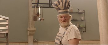 Movie still from “Paddington 2” (2017), directed by Paul King – An old man with a beard wearing an apron and a chef's hat; Close Up shot, Low angle