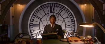 Movie still from “Paddington 2” (2017), directed by Paul King – A man holding a book in front of a large clock; Medium shot, Low angle