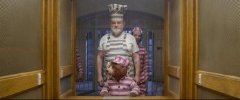 Movie still from “Paddington 2” (2017), directed by Paul King – A man and a woman in prison uniforms with a bear; Medium shot, Low angle
