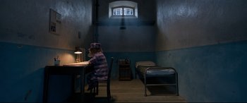 Movie still from “Paddington 2” (2017), directed by Paul King – A person sitting at a table in a room with a bed; Wide shot, High angle