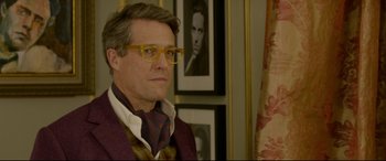 Movie still from “Paddington 2” (2017), directed by Paul King – A man wearing glasses and a tie in front of a portrait; Close Up shot, Over the shoulder angle