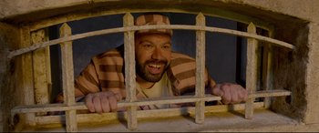 Movie still from “Paddington 2” (2017), directed by Paul King – A man with a beard and striped shirt looking through a window; Medium shot, Overhead angle