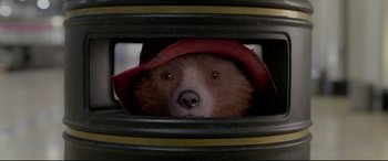 Movie still from “Paddington 2” (2017), directed by Paul King – A brown bear wearing a red hat looking through a hole in the wall; Close Up shot, Overhead angle
