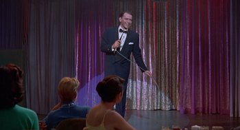 Movie still from “Pal Joey” (1957), directed by George Sidney – A man in a tuxedo is holding a microphone; Wide shot, Over the shoulder angle