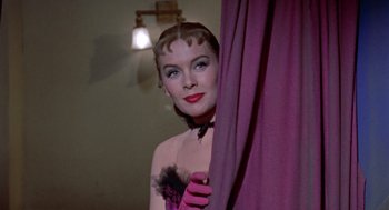 Movie still from “Pal Joey” (1957), directed by George Sidney – A woman in a pink dress and pink gloves looking over a curtain; Close Up shot, Low angle