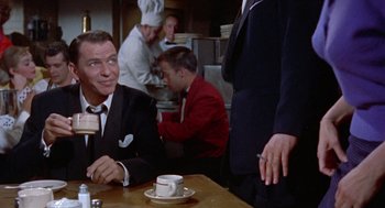Movie still from “Pal Joey” (1957), directed by George Sidney – A man sitting at a table in front of two other men; Medium shot, Over the shoulder angle