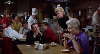 Movie still from “Pal Joey” (1957), directed by George Sidney – A group of people sitting at a table eating food; Medium shot, Over the shoulder angle