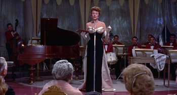 Movie still from “Pal Joey” (1957), directed by George Sidney – A woman in a black and white dress is singing; Medium shot, Low angle