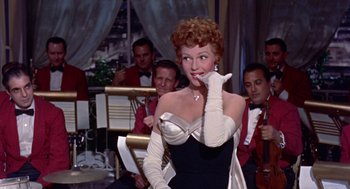 Movie still from “Pal Joey” (1957), directed by George Sidney – A woman in a black and white dress with a microphone; Medium shot, Over the shoulder angle