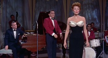 Movie still from “Pal Joey” (1957), directed by George Sidney – A man and a woman standing next to each other in front of a piano; Medium shot, Low angle