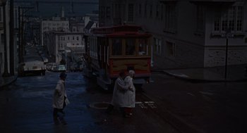 Movie still from “Pal Joey” (1957), directed by George Sidney – Two women are hugging on the sidewalk near a trolley; Extreme Wide shot, High angle