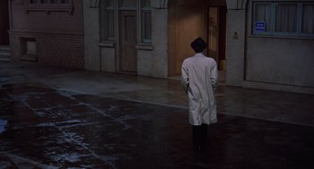 Movie still from “Pal Joey” (1957), directed by George Sidney – A man in a white coat is standing in the rain; Wide shot, High angle