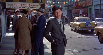 Movie still from “Pal Joey” (1957), directed by George Sidney – A man in a suit and hat standing on a sidewalk; Medium shot, Over the shoulder angle