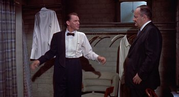 Movie still from “Pal Joey” (1957), directed by George Sidney – A man wearing a suit and tie talking to another man; Medium shot, Over the shoulder angle