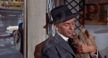 Movie still from “Pal Joey” (1957), directed by George Sidney – A man wearing a suit and hat holding a dog; Close Up shot, Low angle