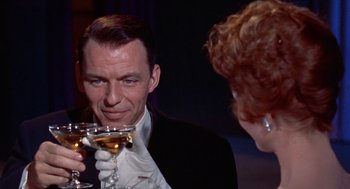 Movie still from “Pal Joey” (1957), directed by George Sidney – A man and a woman holding wine glasses in front of him; Close Up shot, Over the shoulder angle