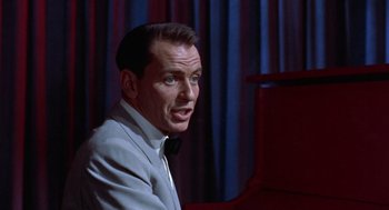 Movie still from “Pal Joey” (1957), directed by George Sidney – A man wearing a suit and bow tie sitting in front of a piano; Close Up shot, Low angle