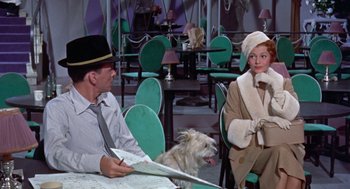 Movie still from “Pal Joey” (1957), directed by George Sidney – A man and a woman sitting at a table with a dog; Medium shot, High angle