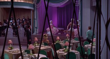 Movie still from “Pal Joey” (1957), directed by George Sidney – A couple of people are sitting at a table in a room; Wide shot, High angle