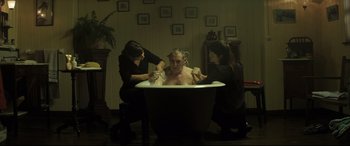 Movie still from “Palm Trees in the Snow” (2015), directed by Fernando González Molina – A man sitting in a bath tub surrounded by two women; Medium shot, High angle