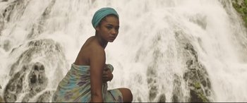 Movie still from “Palm Trees in the Snow” (2015), directed by Fernando González Molina – A woman wrapped in a towel in front of a waterfall; Medium shot, Low angle