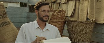 Movie still from “Palm Trees in the Snow” (2015), directed by Fernando González Molina – A man with glasses is writing on a piece of paper; Close Up shot, Over the shoulder angle