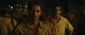 Movie still from “Palm Trees in the Snow” (2015), directed by Fernando González Molina – Two men standing next to each other in the dark; Medium shot, Over the shoulder angle