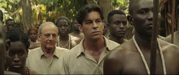 Movie still from “Palm Trees in the Snow” (2015), directed by Fernando González Molina – A group of men standing next to each other in a forest; Medium shot, Over the shoulder angle
