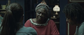 Movie still from “Palm Trees in the Snow” (2015), directed by Fernando González Molina – An older woman in a red shirt is looking at the camera; Close Up shot, Over the shoulder angle