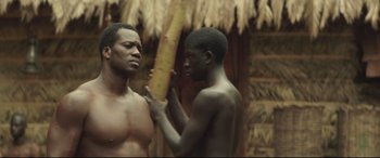 Movie still from “Palm Trees in the Snow” (2015), directed by Fernando González Molina – Two young men standing next to each other in front of a tree; Medium shot, Over the shoulder angle