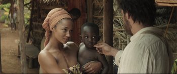 Movie still from “Palm Trees in the Snow” (2015), directed by Fernando González Molina – A woman holding a baby and a man in a straw hut; Close Up shot, Over the shoulder angle