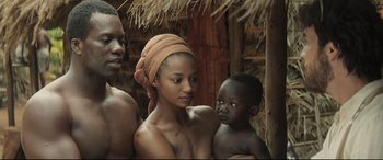 Movie still from “Palm Trees in the Snow” (2015), directed by Fernando González Molina – A woman and two men are standing in a hut; Medium shot, Over the shoulder angle