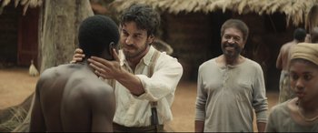 Movie still from “Palm Trees in the Snow” (2015), directed by Fernando González Molina – A man in a white shirt is touching another man's face; Medium shot, Over the shoulder angle