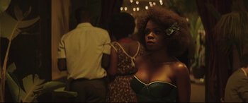 Movie still from “Palm Trees in the Snow” (2015), directed by Fernando González Molina – A woman in a green dress standing in front of other people; Medium shot, Over the shoulder angle
