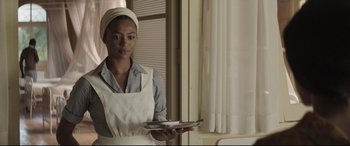 Movie still from “Palm Trees in the Snow” (2015), directed by Fernando González Molina – A woman holding a tray in a kitchen; Medium shot, Over the shoulder angle