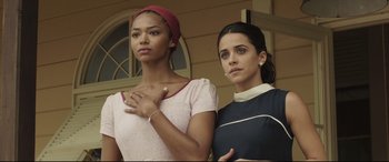 Movie still from “Palm Trees in the Snow” (2015), directed by Fernando González Molina – Two women standing next to each other in front of a building; Medium shot, Low angle