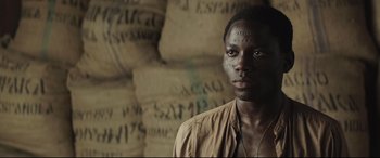 Movie still from “Palm Trees in the Snow” (2015), directed by Fernando González Molina – A man standing in front of a wall of bags; Close Up shot, High angle