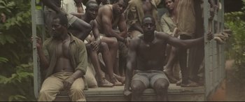 Movie still from “Palm Trees in the Snow” (2015), directed by Fernando González Molina – A group of men sitting next to each other on the ground; Medium shot, High angle