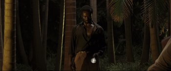 Movie still from “Palm Trees in the Snow” (2015), directed by Fernando González Molina – A man holding a flashlight while standing next to a tree; Medium shot, High angle