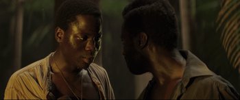 Movie still from “Palm Trees in the Snow” (2015), directed by Fernando González Molina – Two men are facing each other in the dark; Close Up shot, Over the shoulder angle