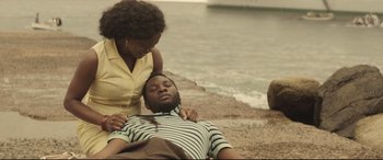 Movie still from “Palm Trees in the Snow” (2015), directed by Fernando González Molina – A man laying on the ground next to a woman on the beach; Medium shot, High angle
