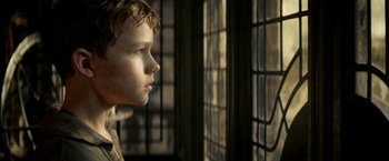 Movie still from “Pan” (2015), directed by Joe Wright – A young boy looking out of a stained glass window; Close Up shot, Over the shoulder angle