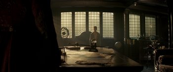Movie still from “Pan” (2015), directed by Joe Wright – A man sitting at a table in a room with stained glass windows; Wide shot, Low angle