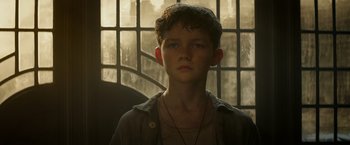 Movie still from “Pan” (2015), directed by Joe Wright – A young boy with a necklace in front of a window; Close Up shot, Low angle