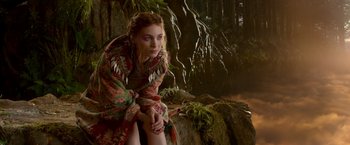 Movie still from “Pan” (2015), directed by Joe Wright – A woman sitting on top of a rock in front of trees; Medium shot, Over the shoulder angle