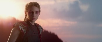 Movie still from “Pan” (2015), directed by Joe Wright – A young woman with pink eye shadow is standing in front of a sunset; Close Up shot, Over the shoulder angle