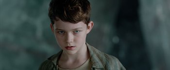 Movie still from “Pan” (2015), directed by Joe Wright – A young boy with blue eyes stares into the camera; Close Up shot, Over the shoulder angle
